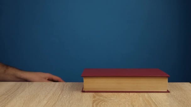 το χέρι βάζει τα βιβλία το ένα πάνω στο άλλο σε ένα μπλε φόντο. Εκπαιδευτική και μαθησιακή έννοια. - Πλάνα, βίντεο