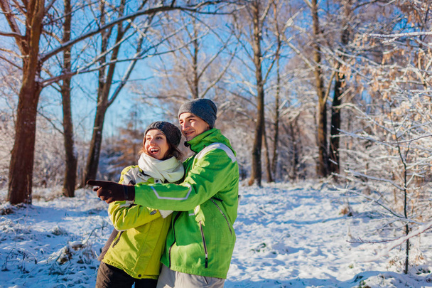 Winter activities. Couple in love walking and hugging in winter forest. Young people pointing and looking at something - Photo, Image