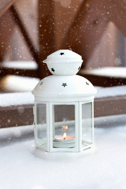 White Christmas lantern in snow, with yellow candle light, on wooden background - Foto, afbeelding
