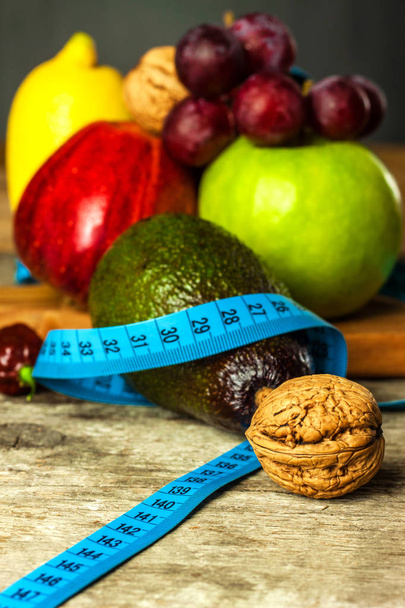 コンセプトダイエット。健康食品。木製のテーブルの上に測定テープで包まれた木製のボード上の果物。重量損失の概念. - 写真・画像