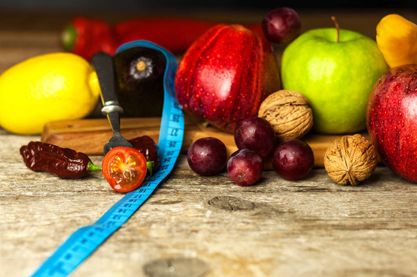 Konsept diyet. Sağlıklı yiyecekler. Tahta bir tahtanın üzerindeki meyveler ahşap bir masada mezura ile sarılmış. Kilo kaybı kavramı. - Fotoğraf, Görsel
