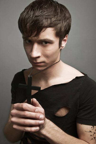 Young man in modern black clothing holding big black cross in hands - Φωτογραφία, εικόνα