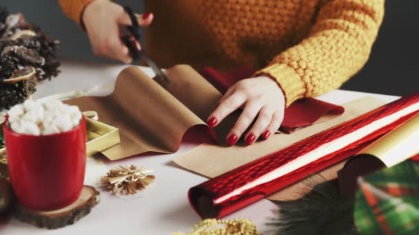 Donna che taglia carta rossa per avvolgere regali di Natale in tavola con decorazione natalizia
. - Filmati, video