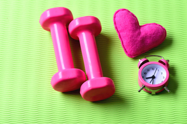 Dumbbells in pink color next to alarm clock and heart - Foto, imagen