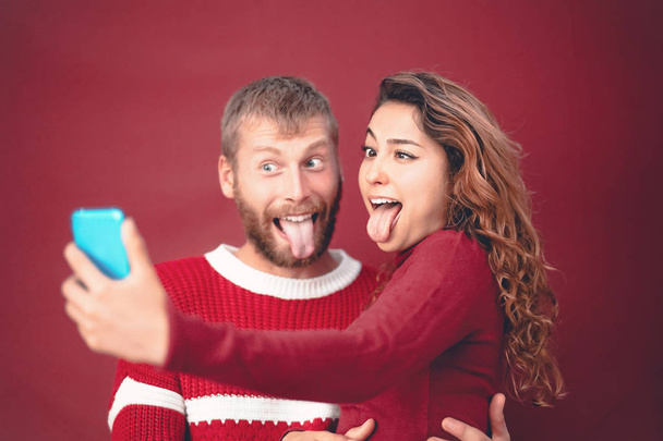 Feliz casal louco tirar selfie ao fazer cara boba com câmera de smartphone móvel - Jovens comemorando feriados de Natal - Relacionamento amoroso, xmas e conceito de tendências tecnológicas
 - Foto, Imagem