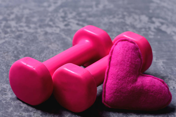 Dumbbells made of pink plastic near soft toy heart - Photo, Image