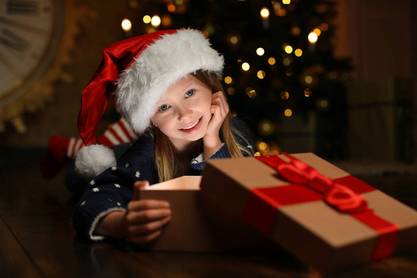 Cute child opening magic gift box near Christmas tree at night - Foto, Imagem