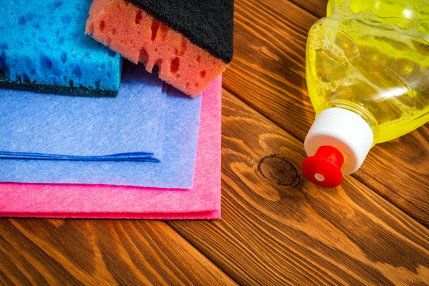 Détergent liquide avec tampons et serviettes de différentes couleurs pour le nettoyage sur des planches en bois
 - Photo, image