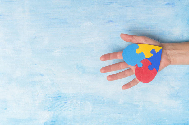 Ręka trzymając kolorowe serce na niebieskim tle. Koncepcja Światowego Dnia Świadomości Autyzmu - Zdjęcie, obraz