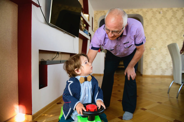 grandfather rolls grandson in a toy car. redirection of grandfather and grandson. Happy weekend concept. Happy grandfather and grandson walk at home. - Фото, изображение