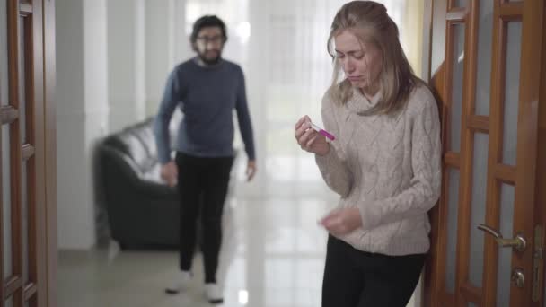Blurred Caucasian man yelling at his girlfriend or wife from background. Depressed woman holding pregnancy test and crying. Unwanted pregnancy, relationship problems. - Materiaali, video