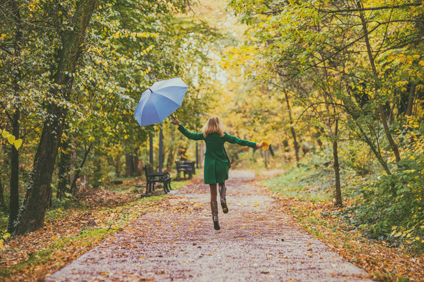 Woman holding umbrella and fall leafs while jumping and  walking in the park. - Фото, изображение