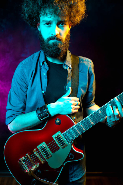 Close-up photo of hipster man with red guitar in neon lights. Rock musician is playing electrical guitar. - Fotoğraf, Görsel