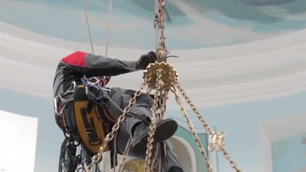 Een industriële klimmer op een ladder bereidt een touw voor op het hijsmateriaal. een werknemer met een beschermhelm breit een knoop aan een touw. - Video