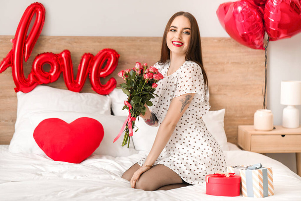 Beautiful young woman with gifts and flowers in bedroom. Valentine's Day celebration - Фото, изображение