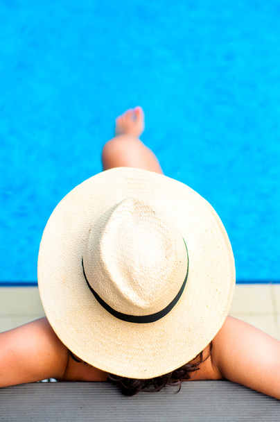 Woman with beach hat relaxing by the pool at exotic resort - Фото, изображение