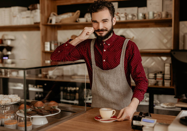 Friendly barista serving cup of coffee at counter in hipster cafe - Foto, Imagem