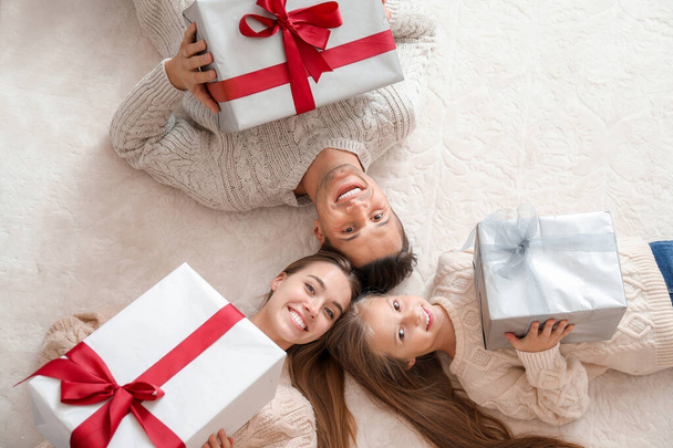 Щаслива молода сім'я з різдвяними подарунками, що лежать на підлозі, вид зверху
 - Фото, зображення