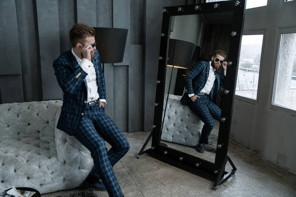 Handsome stylish man in blue suit in a cage at home sitting on sofa near mirror. - Foto, imagen