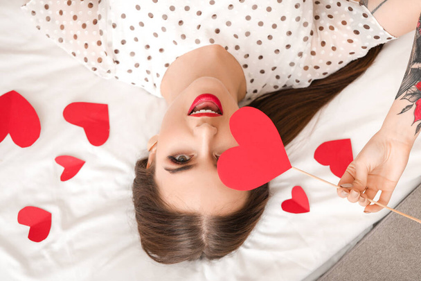 Όμορφη νεαρή γυναίκα με κόκκινες καρδιές ξαπλωμένη στο κρεβάτι. Γιορτή του Αγίου Βαλεντίνου - Φωτογραφία, εικόνα