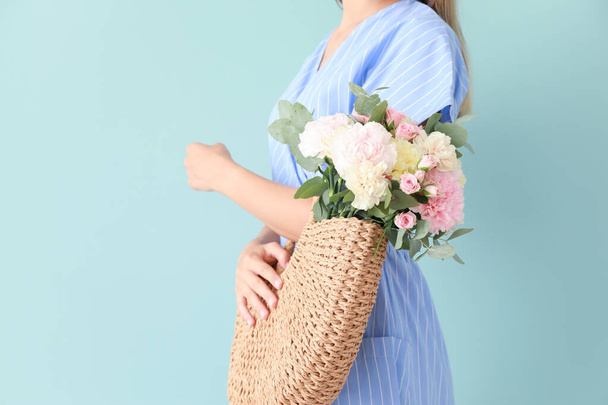 Beautiful young woman with bag and bouquet of carnation flowers on color background - Foto, imagen