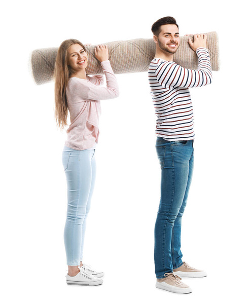 Young couple holding rolled carpet against white background - Foto, immagini
