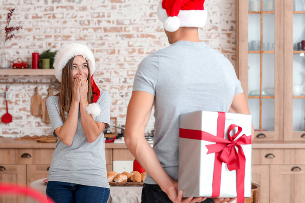 Szczęśliwy młody człowiek daje prezent świąteczny swojej dziewczynie w domu - Zdjęcie, obraz