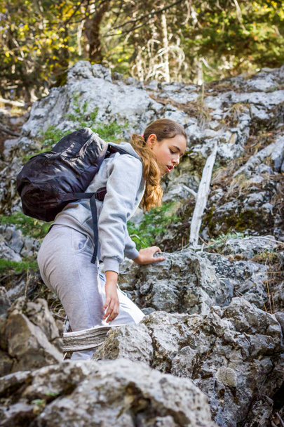 Young teenager girl with trekking poles and a backpack in the forest. Mountain climbing - Foto, imagen