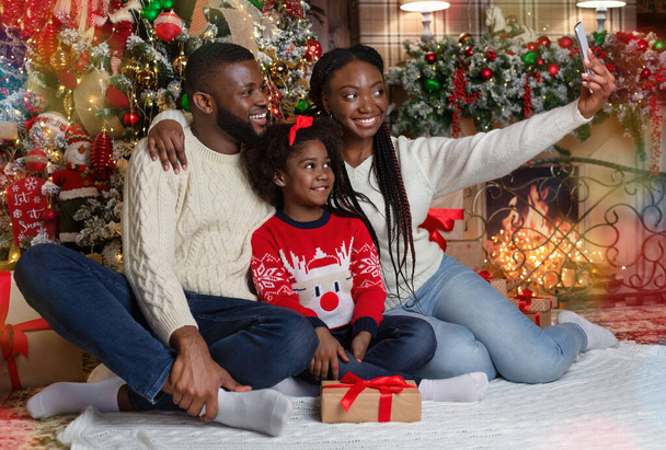 Happy black woman taking Christmas selfie with her husband and daughter - Zdjęcie, obraz