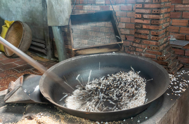 Μαύροι πυρήνες ρυζιού ξεπετάγονται σε μαύρη θερμαινόμενη λεκάνη στο Cai Be, Meko - Φωτογραφία, εικόνα
