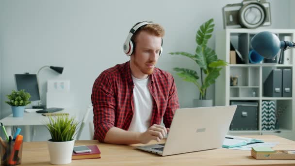 Joyful guy wearing headphones dancing in office working with laptop doing business - Filmmaterial, Video