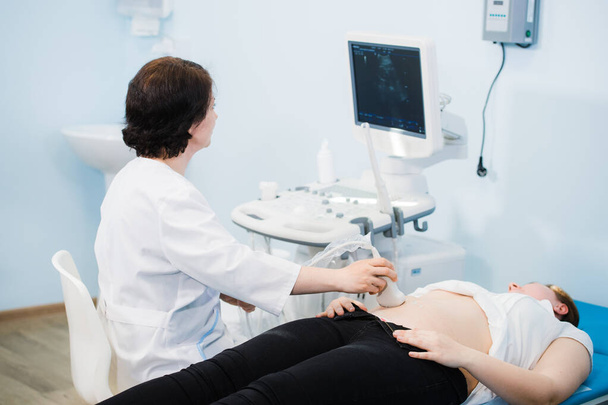 Gelukkig volwassen vrouwelijke arts met behulp van ultrasone scanner. echografie machine - Foto, afbeelding