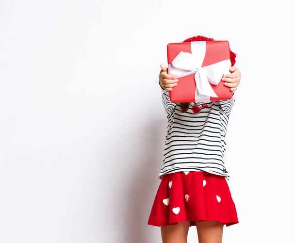 Happy cute young girl holding a red gift box with a white ribbon over a light background - Fotó, kép