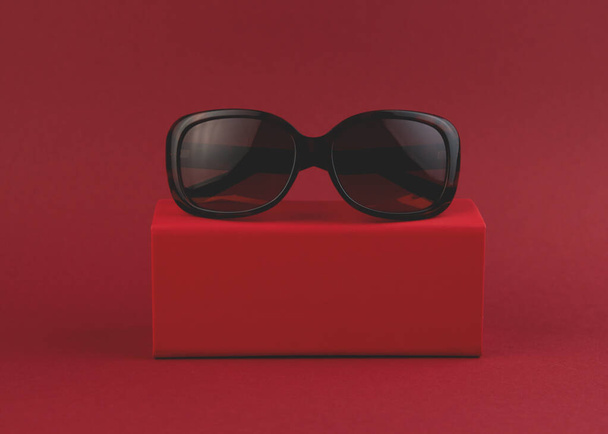 Óculos de sol na moda em uma caixa em um contexto vermelho. Estilo mínimo. Foto de moda minimalista
. - Foto, Imagem