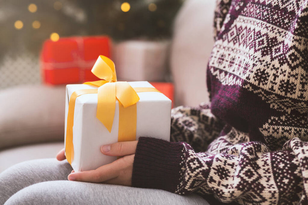 Γυναίκα κρατώντας χριστουγεννιάτικο δώρο στα χέρια και κάθεται στον καναπέ - Φωτογραφία, εικόνα