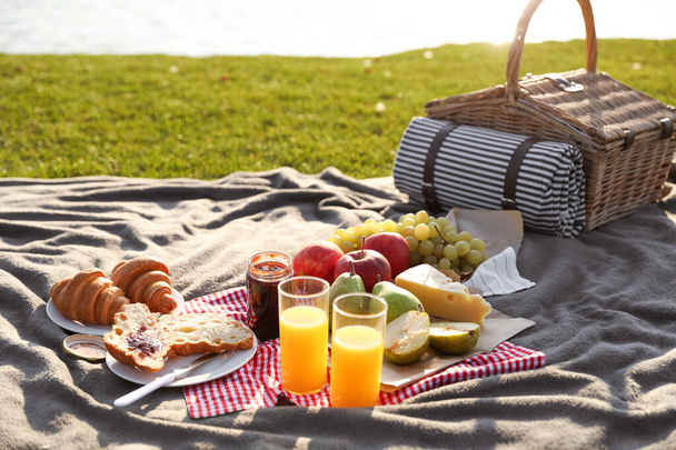 Picknickdeken met heerlijk eten en sap buiten op zonnige dag - Foto, afbeelding