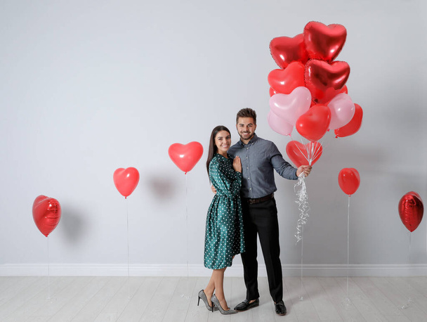 Happy young couple with heart shaped balloons near light wall. Valentine's day celebration - Foto, Imagem