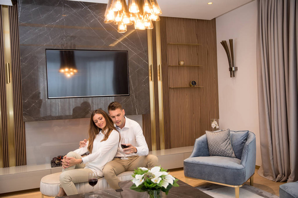 Young couple having a romantic evening with a glass of red wine at home in the luxury contemporary living room - Fotografie, Obrázek