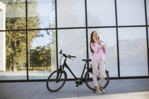 Όμορφη νεαρή γυναίκα που χρησιμοποιεί το κινητό τηλέφωνο από τη σύγχρονη πόλη ηλεκτρικό e-bike ως καθαρή βιώσιμη αστική μεταφορά - Φωτογραφία, εικόνα