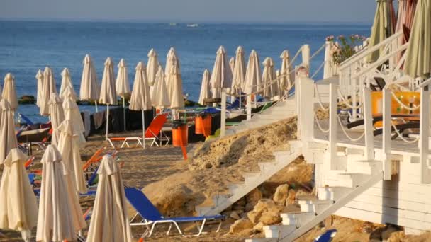 Un sacco di sedie a sdraio multicolore vuote e ombrelloni piegati sulla spiaggia resort in riva al mare, in un resort
 - Filmati, video