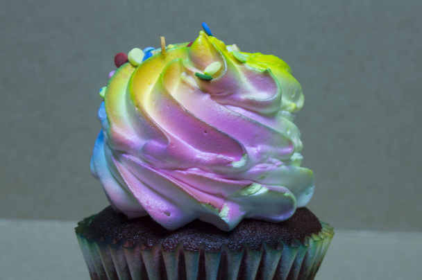 This is a photograph of a Red Velvet cupcake topped with colorful frosting and sprinkles - Photo, Image
