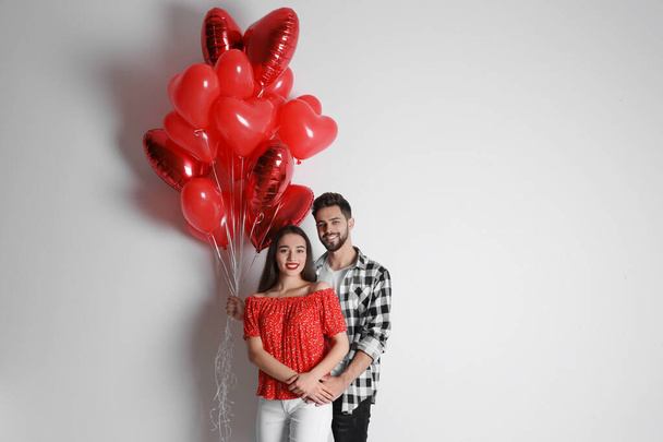 Happy young couple with heart shaped balloons on light background. Valentine's day celebration - Fotoğraf, Görsel