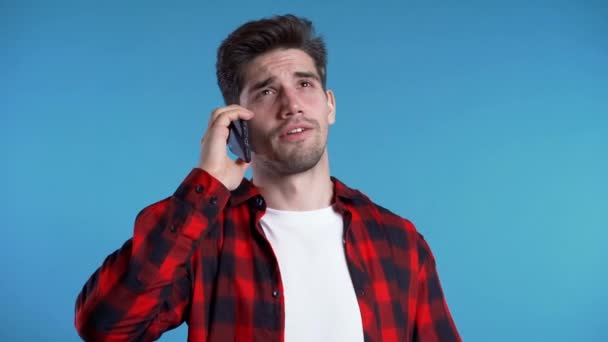 Young man in red wear talking on mobile phone on blue background. Trendy guy have conversation. Smartphone, technology concept. - Кадры, видео