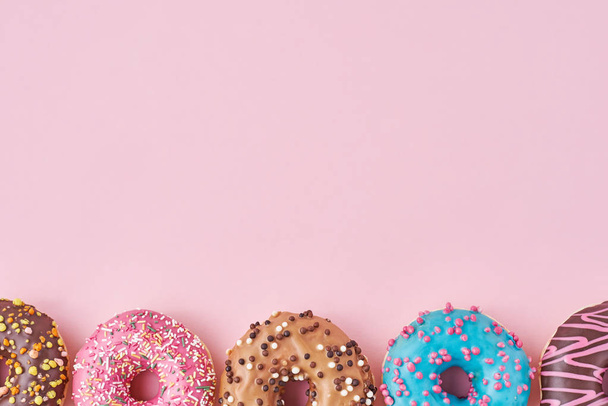 Different types of a colorful donats decorated sprinkles and icing on pastel pink background with copy space - Φωτογραφία, εικόνα