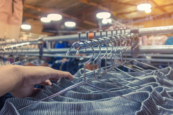Mensen controleren en kiezen broek te kopen op hangers in een kledingwinkel. - Foto, afbeelding