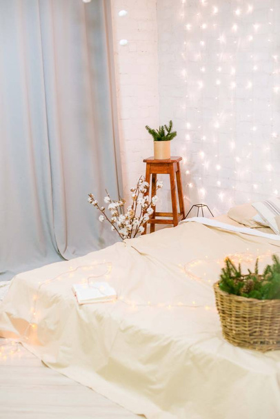 Bright bedroom with a large bright bed, in a loft style decorated with garlands and baskets with needles and cotton branches. New Year 2020. Christmas mood - Fotó, kép