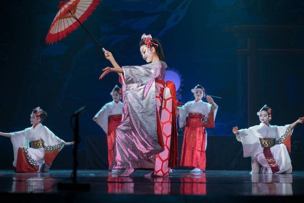 Tradycyjny japoński występ. Aktorki w tradycyjnym białym i czerwonym kimono i maskach lisa tańczące z parasolem i fanami. - Zdjęcie, obraz