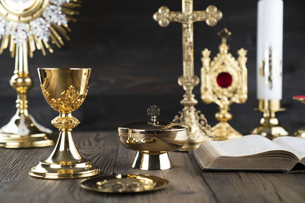 Roman Catholic Church theme. The Cross, Holy Bible, monstrance, rosary and golden chalice on rustic wooden table. - Photo, Image