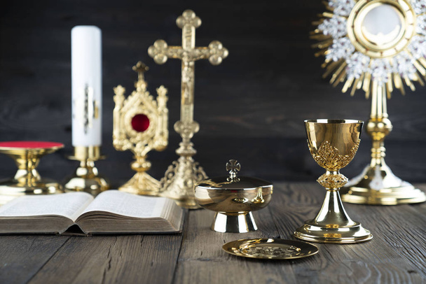 Thema der römisch-katholischen Kirche. Kreuz, Bibel, Monstranz, Rosenkranz und goldener Kelch auf rustikalem Holztisch. - Foto, Bild