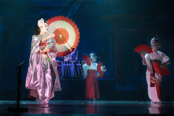 Actuación tradicional japonesa. Actrices en tradicional kimono blanco y rojo y máscaras de zorro bailando con paraguas y abanicos
. - Foto, imagen